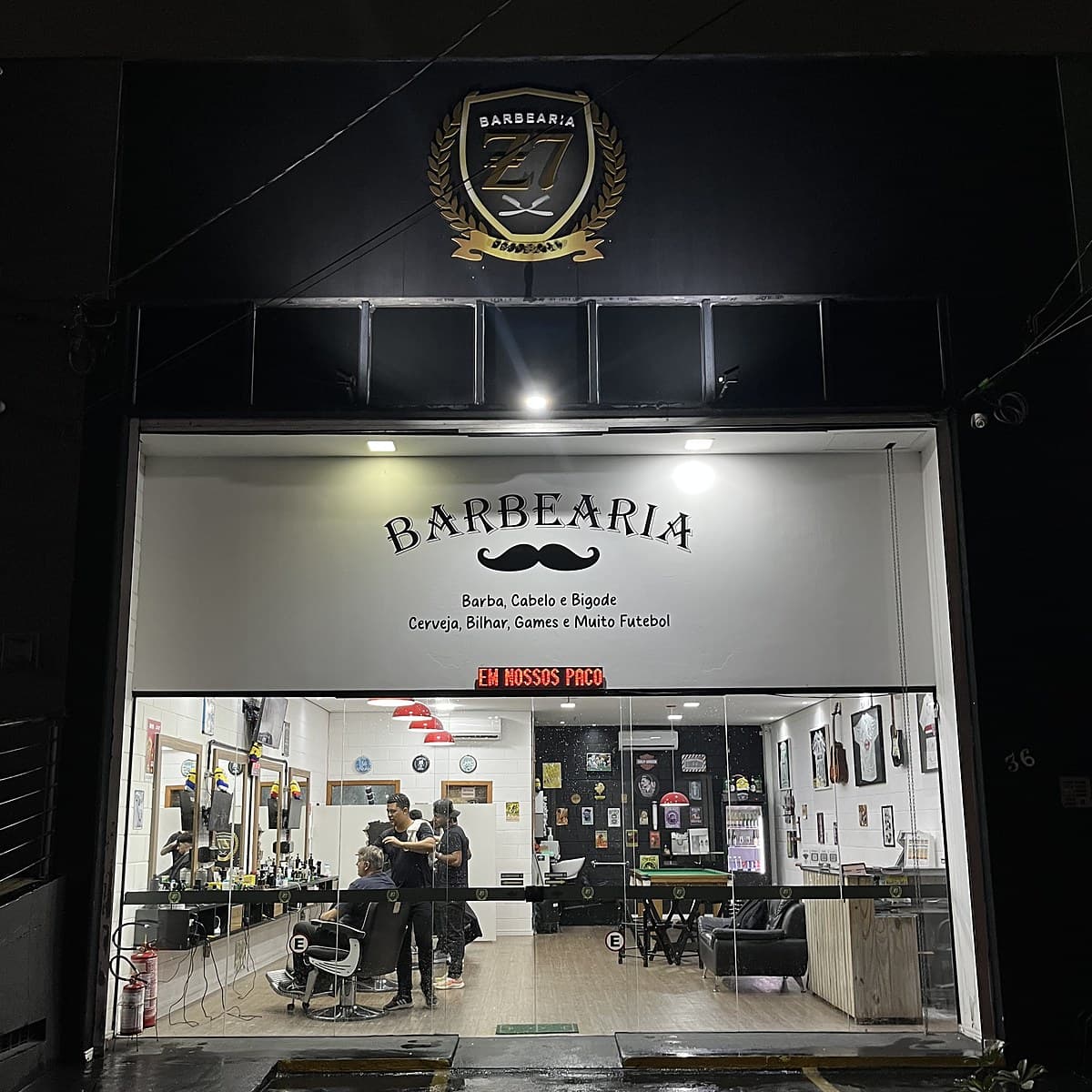 Fachada da Z7 Barbearia à noite, com o brasão iluminado, no Alto Ipiranga em Mogi das Cruzes